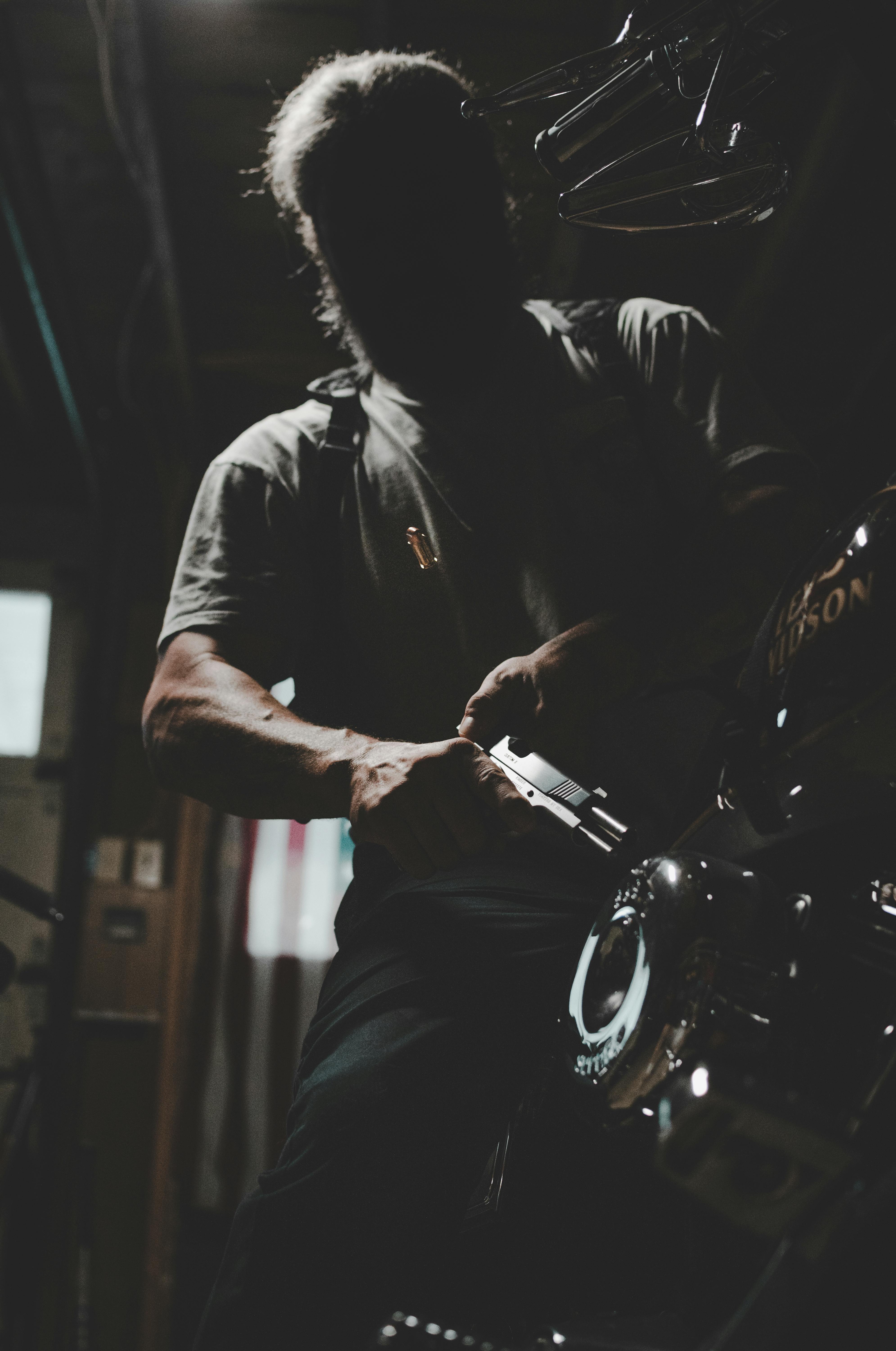 A dramatic silhouette of a man working on a motorcycle inside a dimly lit garage.